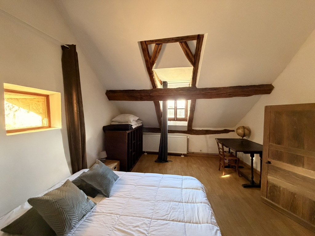 Attic bedroom with sloped ceiling, beams, and a desk by the window