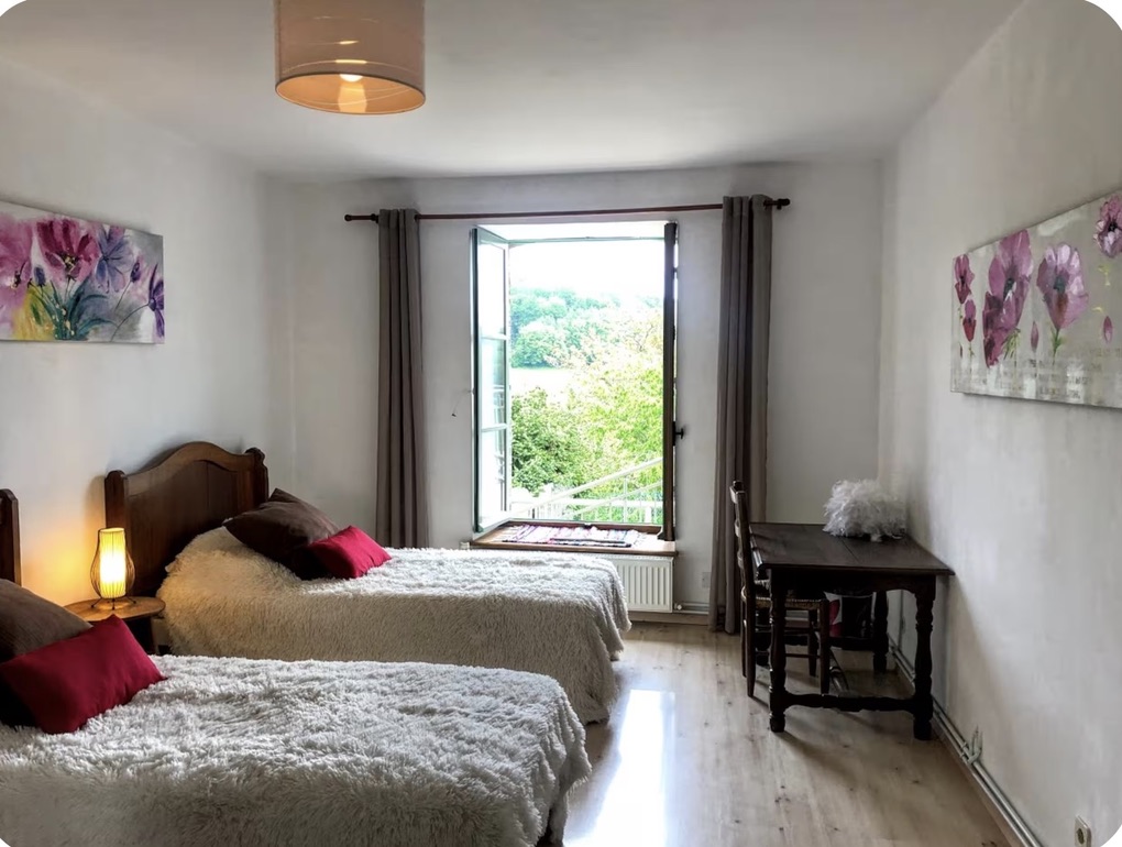 Bright bedroom with two beds and a window opening onto the trees