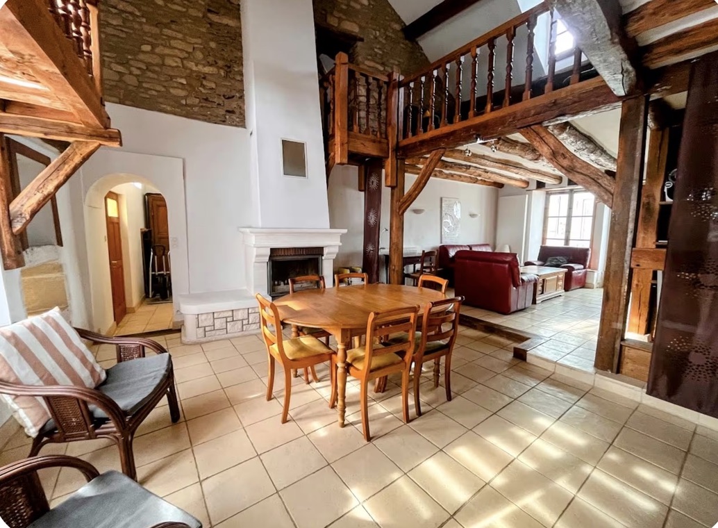 Living room with fireplace, wooden beams, and dining table
