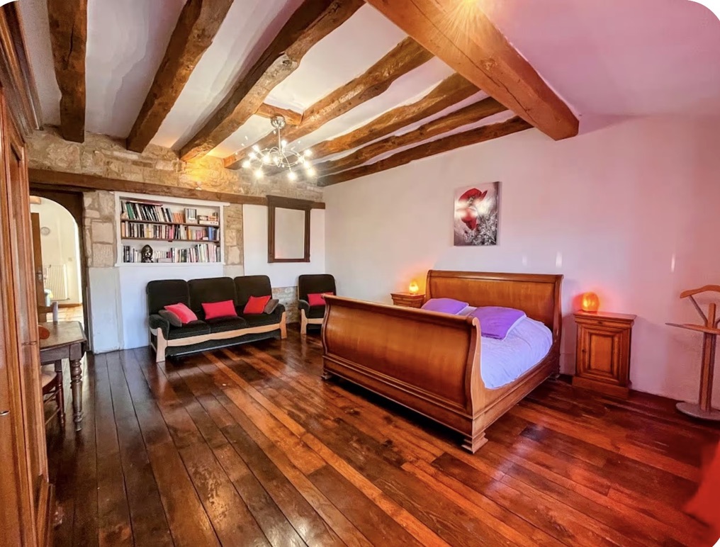 Bedroom with exposed beams, stone wall, and wood floors